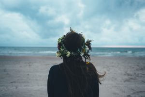 mujer de espaldas sola en la playa con corona de flores